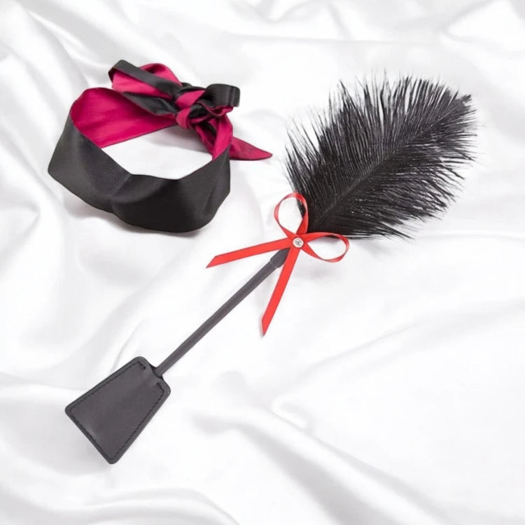 A black satin blindfold and a black flogger with a red bow.