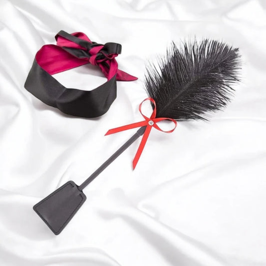 A black satin blindfold and a black flogger with a red bow.